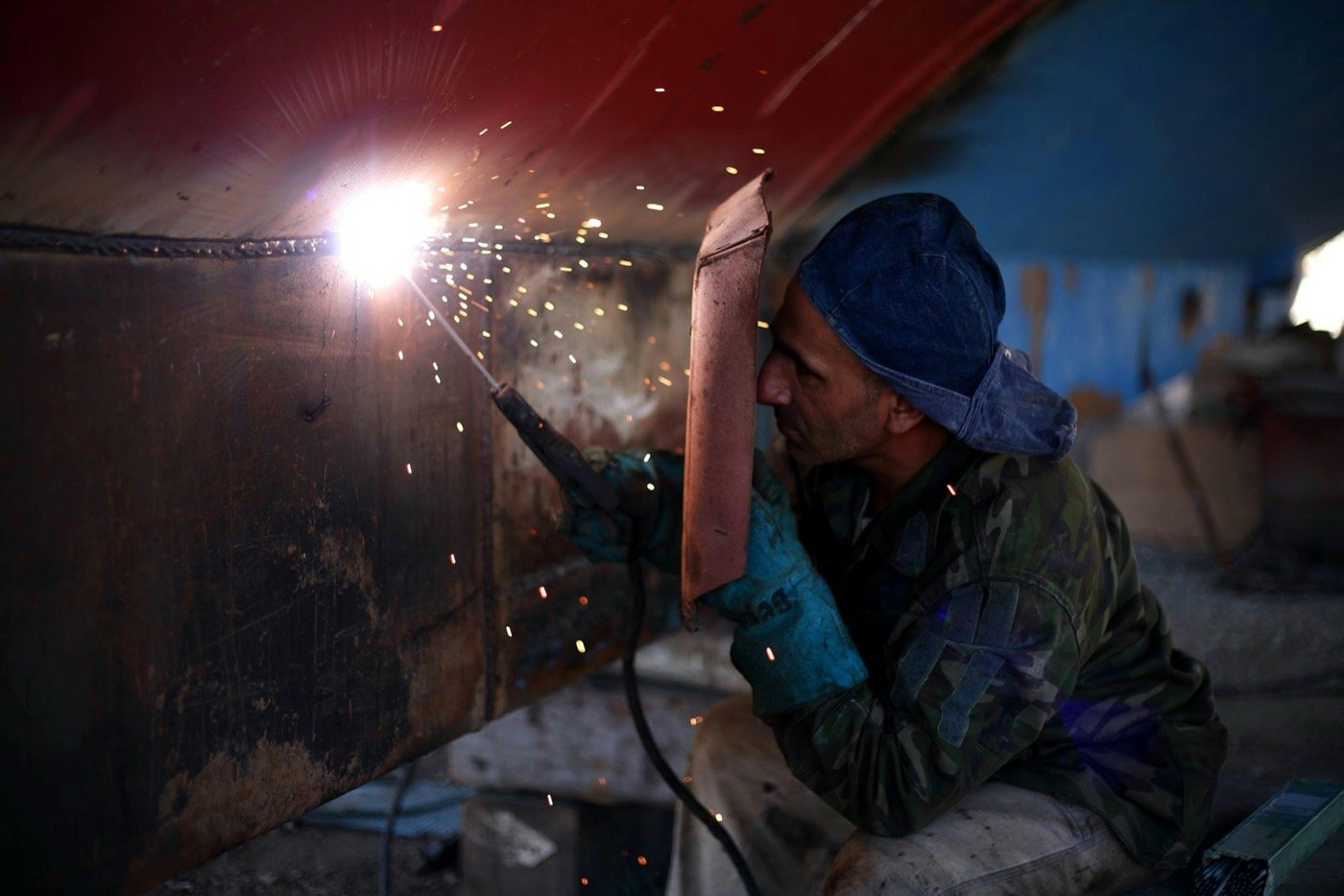 Welder with a handheld shield, sparks flying